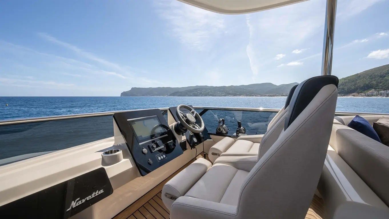 Luxury yacht interior showcasing Navetta dashboard and plush seating, with a panoramic sea view and coastal hills in the background.