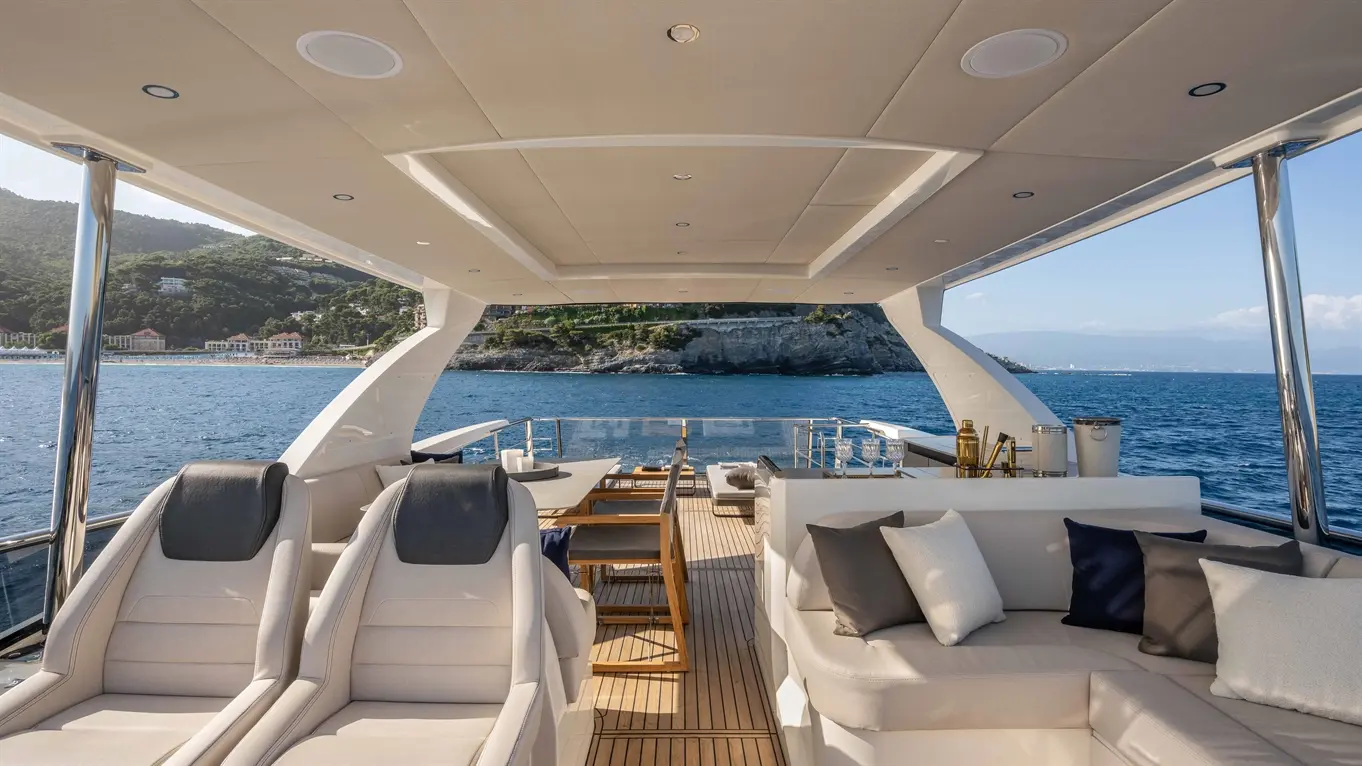 Luxury yacht interior with cushioned seating, sun loungers, and a scenic coastal view over calm waters.