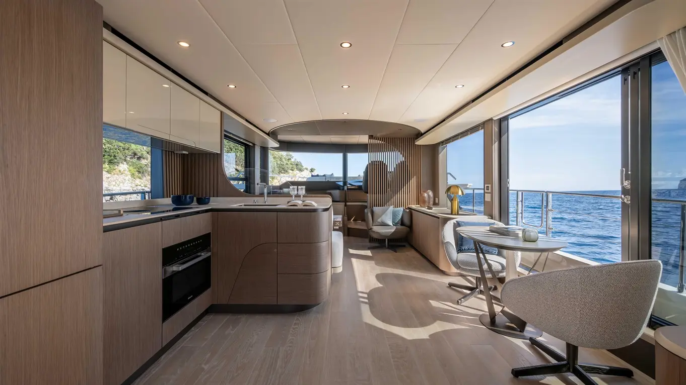 Modern yacht interior featuring a spacious kitchen, dining area, and large windows with views of the sea and coastline.