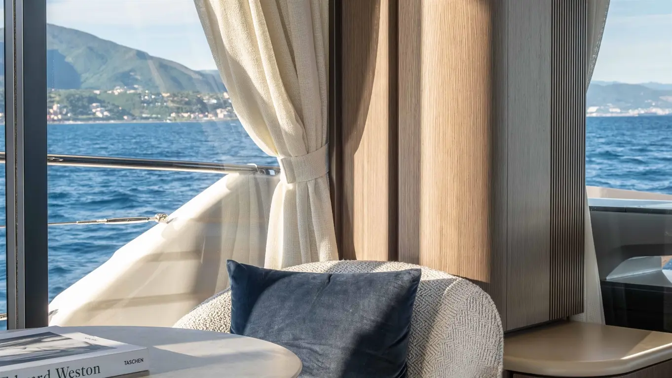 Cozy indoor seating area on a yacht, featuring a round table, a textured armchair with a blue cushion, and scenic views.