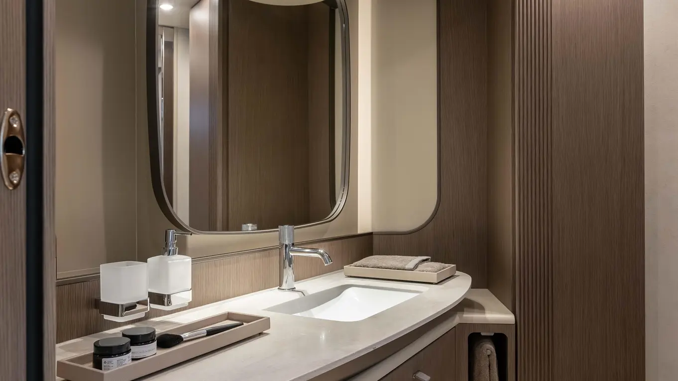 Modern bathroom with a curved vanity, large mirror, sink, storage cabinets, and neatly arranged toiletries on a countertop.
