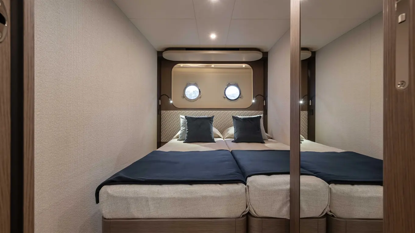 Stylish twin bedroom featuring two beds, navy blue throws, pillows, and round porthole windows for natural light.