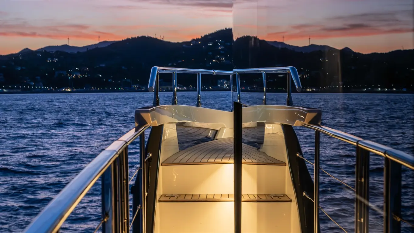 Evening view from a yacht's deck, showcasing a sleek path and calm water under a vibrant sunset sky.