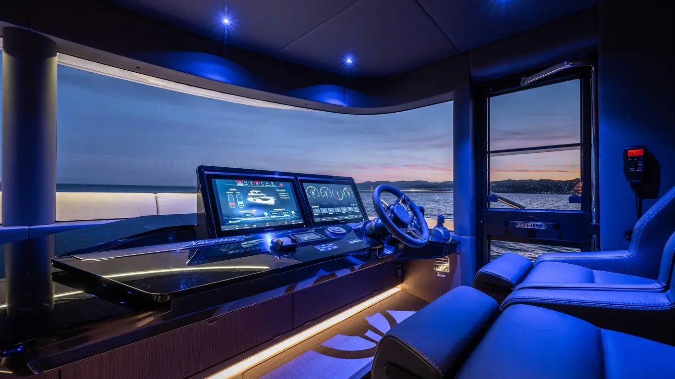 Modern yacht cockpit featuring advanced navigation screens, steering wheel, and blue ambient lighting, overlooking the water.
