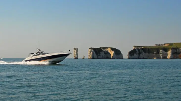 A motorboat speeds through calm waters near white chalk cliffs under a clear blue sky.