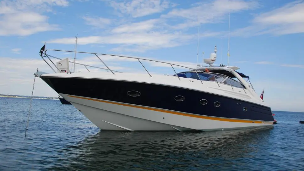 Luxury motorboat anchored in calm waters, featuring a sleek design with a dark blue hull and yellow striping, under a clear sky.