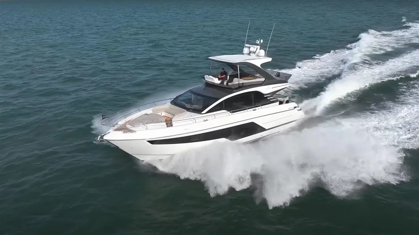 Luxury motor yacht cruising through turquoise waters, creating a spray, with a captain visible at the helm.