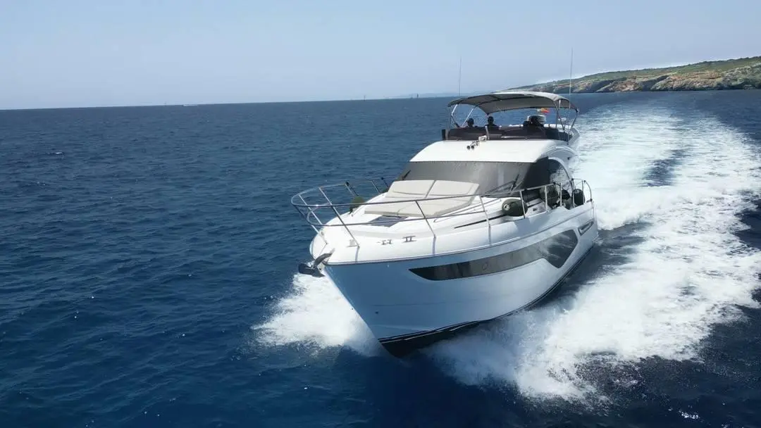 Princess F50 motor yacht cruising across blue sea, leaving a white wake near the rugged coastline.