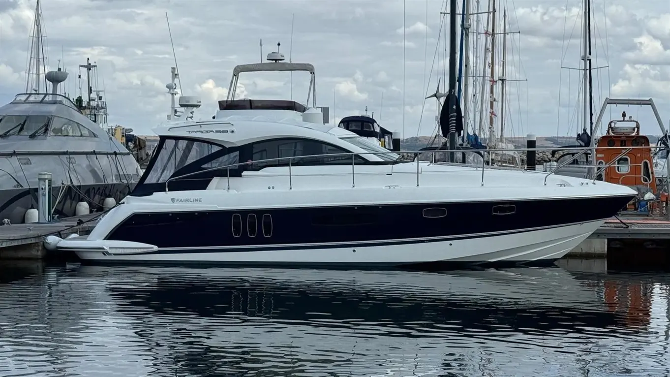 Fairline Targa 38 motor yacht moored in a marina, with sailboats and calm water under cloudy skies.