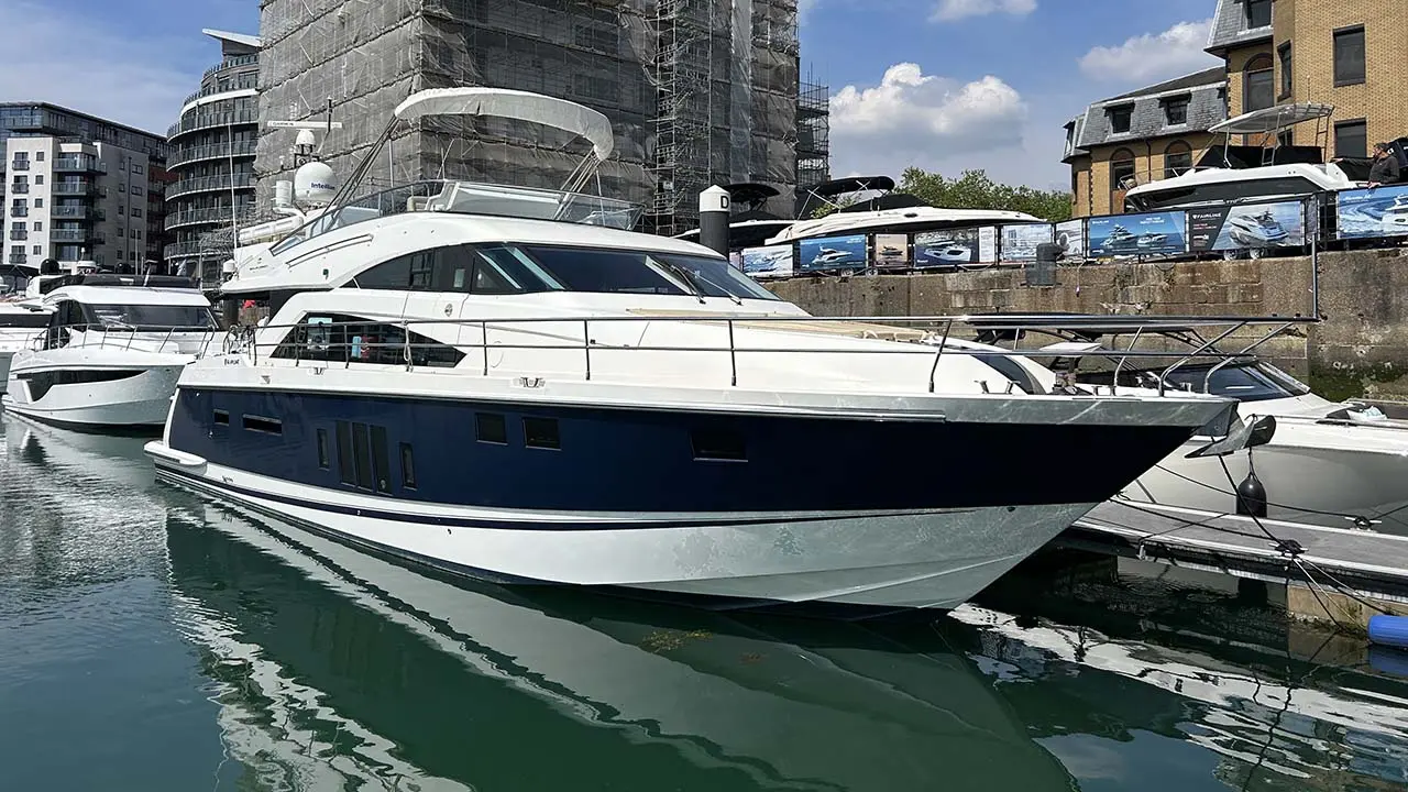 A luxurious motor yacht docked in a marina, surrounded by other boats and modern buildings under a clear blue sky.