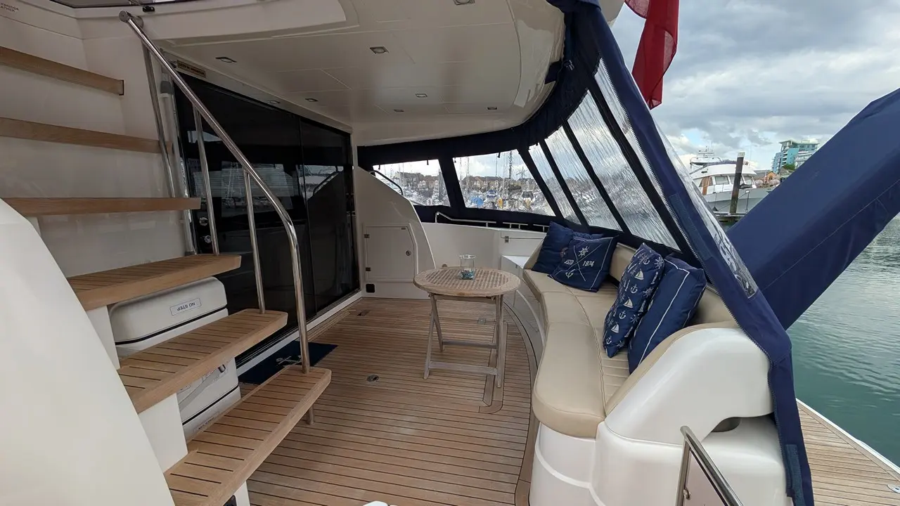 Luxury yacht interior featuring a curved sofa, wooden steps, and a round table with a seaside view. Blue cushions adorn the seating.