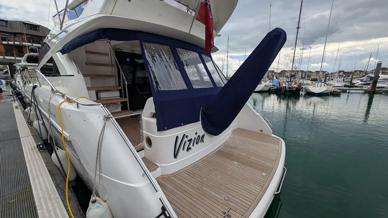 Luxury yacht named "Vizion" docked at a marina, featuring a blue canopy, wooden deck, and surrounding moored boats.