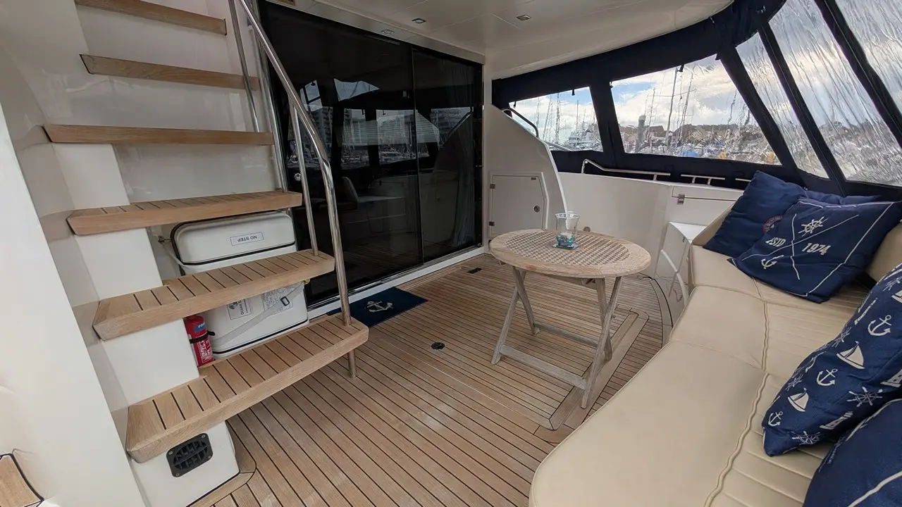 Interior of a boat featuring wooden stairs, a round table with a decorative candle, and cushioned seating with nautical pillows.