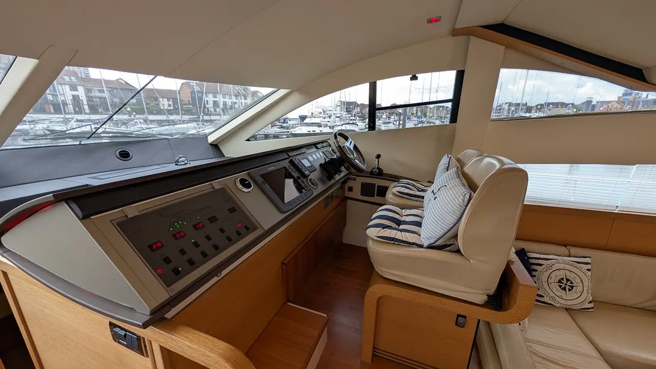 Modern yacht interior featuring a steering wheel, control panel, and comfortable seating with striped cushions, overlooking boats.