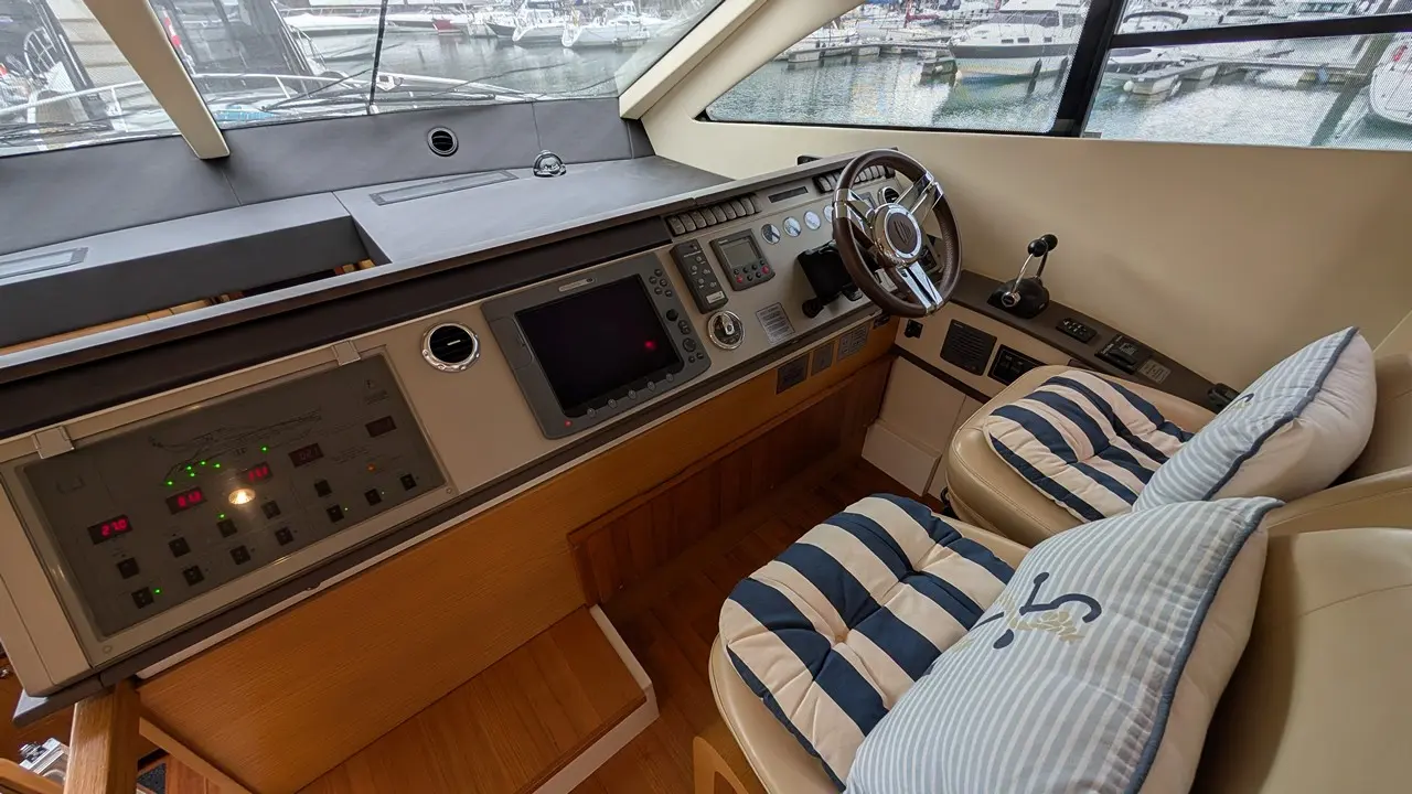 Luxury yacht interior featuring a modern dashboard, steering wheel, and cushioned striped seating, with marina views outside.