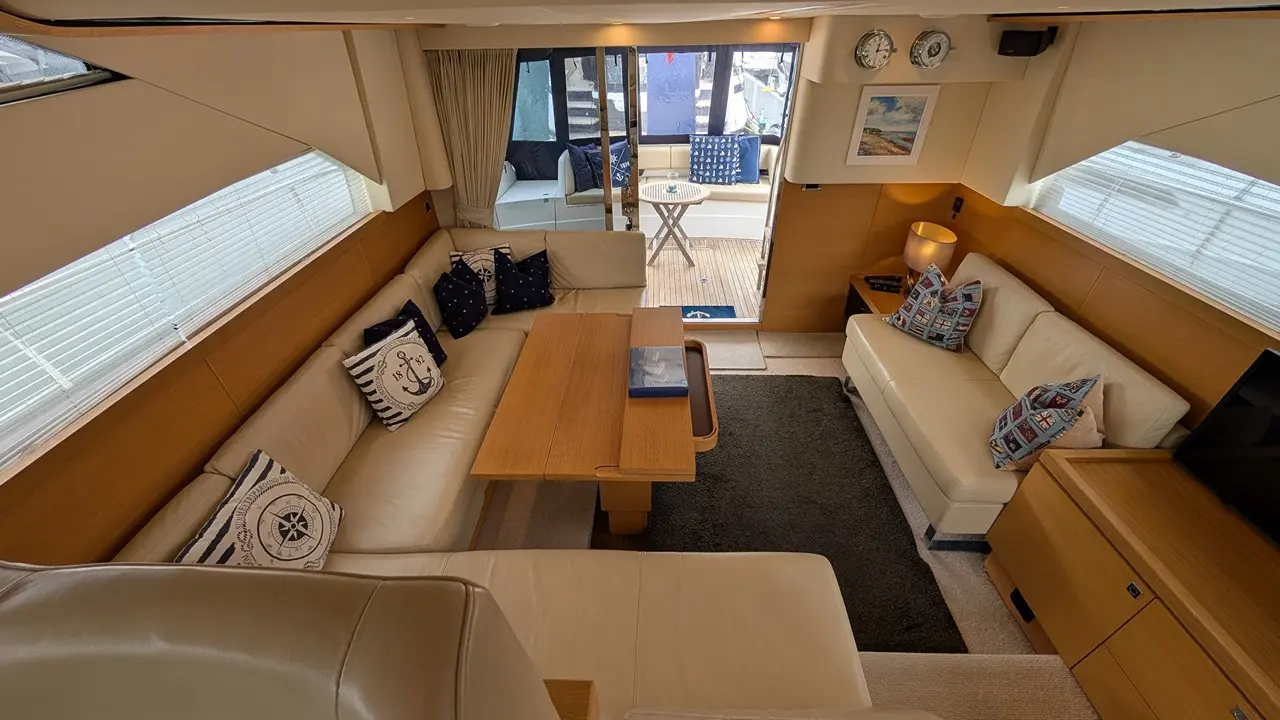 Luxurious boat interior featuring a spacious lounge with cream sofas, nautical cushions, a wooden table, and large windows.