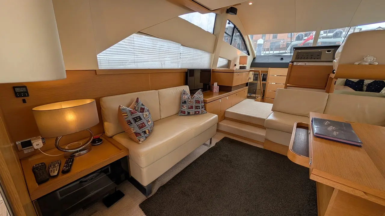Spacious yacht interior with a cream sofa, wooden cabinetry, lamps, and decorative cushions, showcasing modern nautical design.