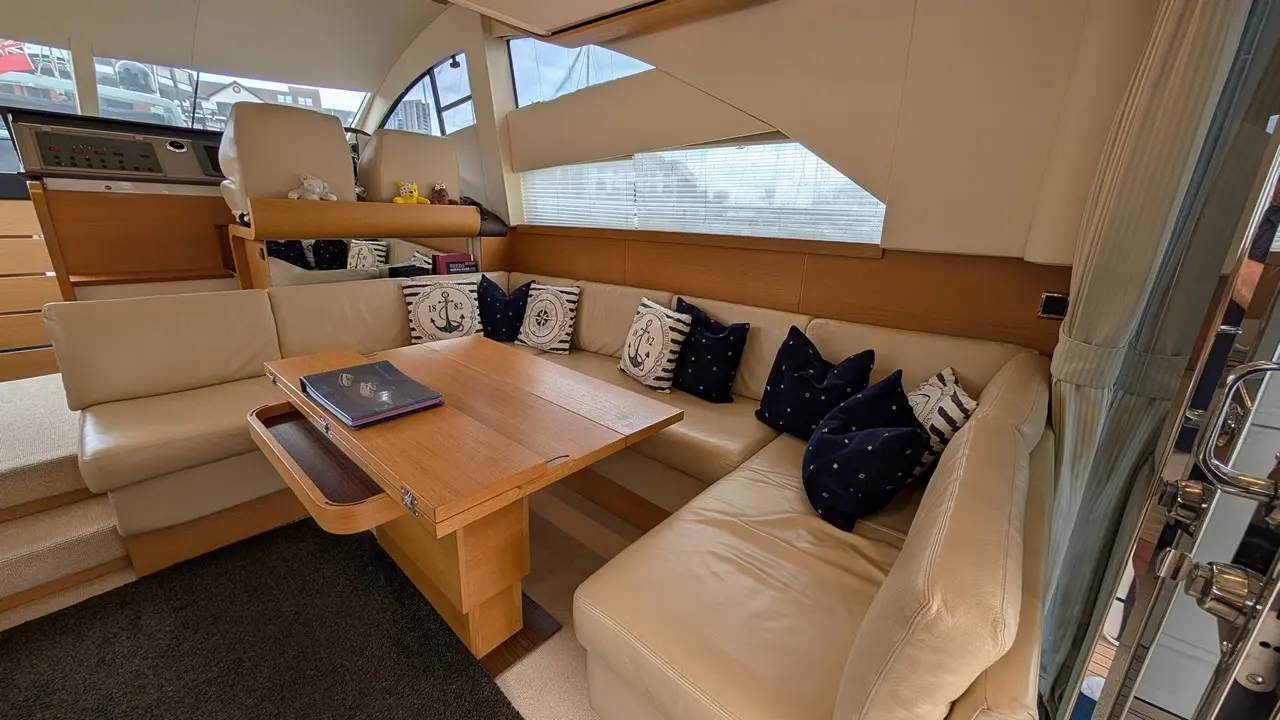 Luxury yacht interior featuring a white leather sofa with nautical-themed cushions and a wooden table, illuminated by natural light.