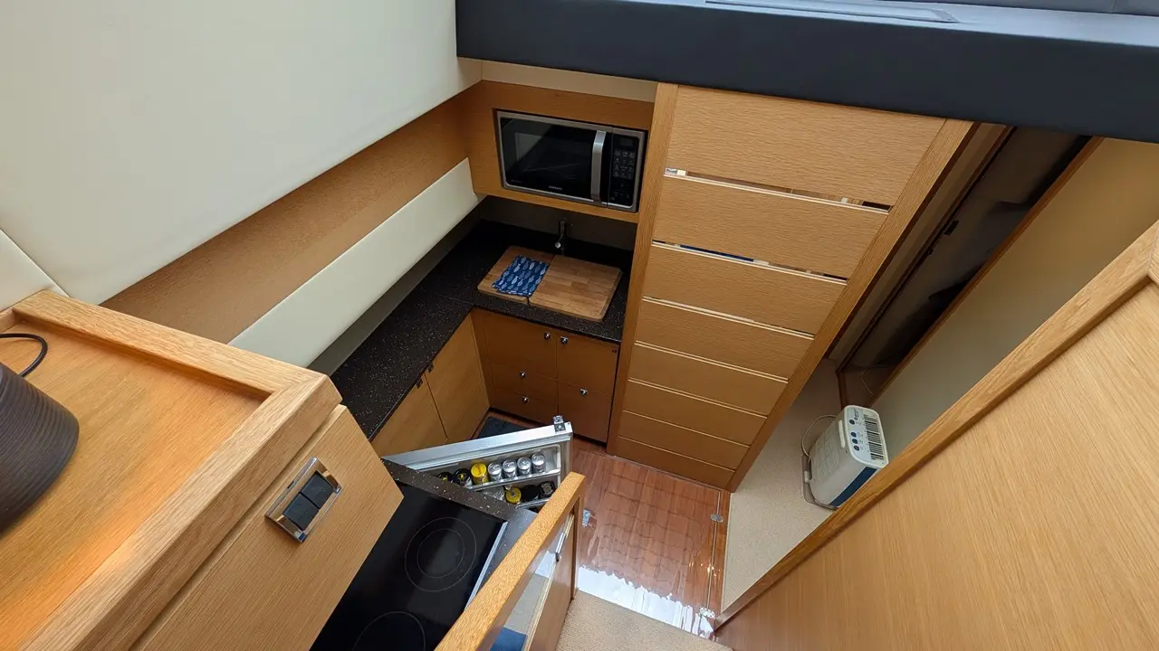Compact kitchen interior featuring a microwave, countertop, cupboards, and a stove, with light wood cabinetry and scroll design.