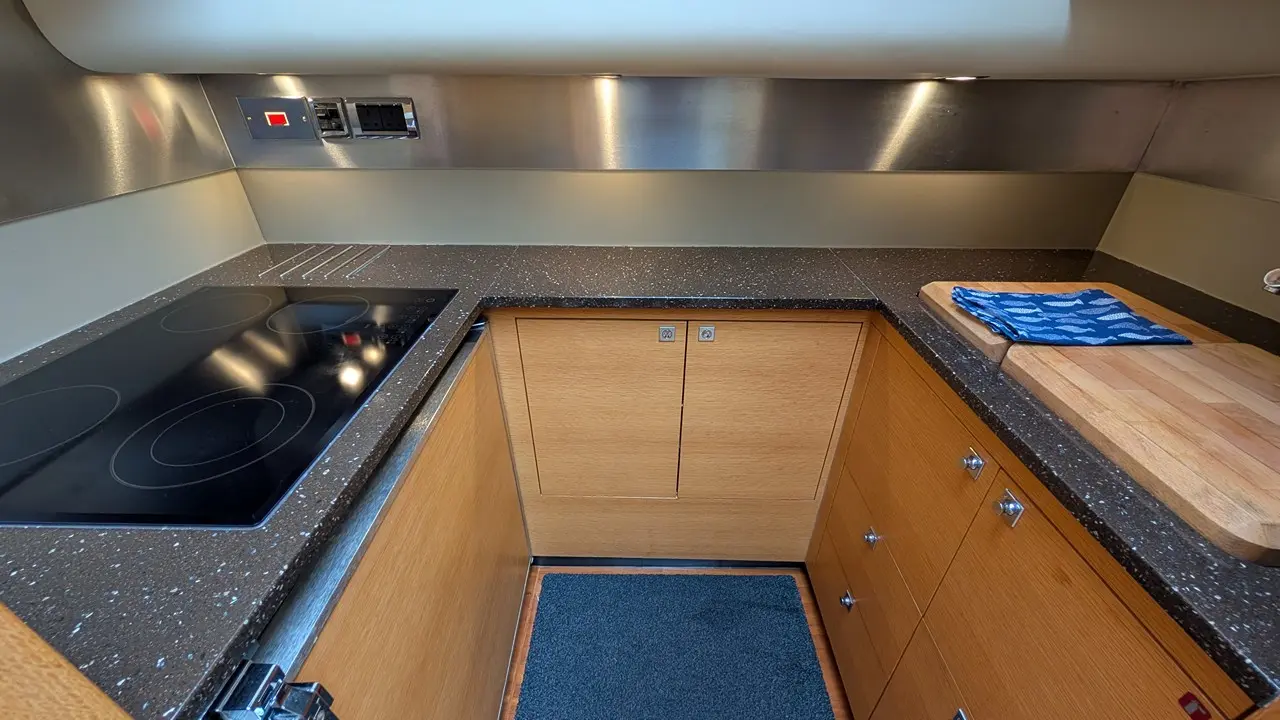Compact kitchen featuring a black induction hob, wooden cabinets, and a cutting board with a blue cloth on the counter.