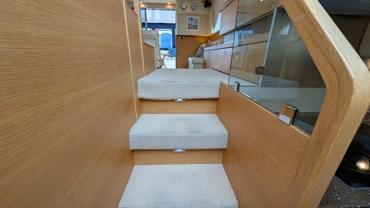 Carpeted stairs lead up to a modern boat interior, featuring wooden walls and glimpses of seating and décor.