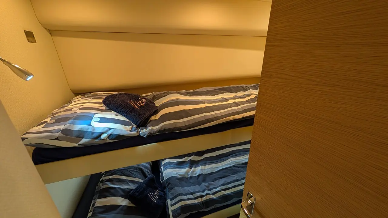 Bunk beds in a compact cabin, featuring striped bedding and a navy towel, visible through an open wooden door.