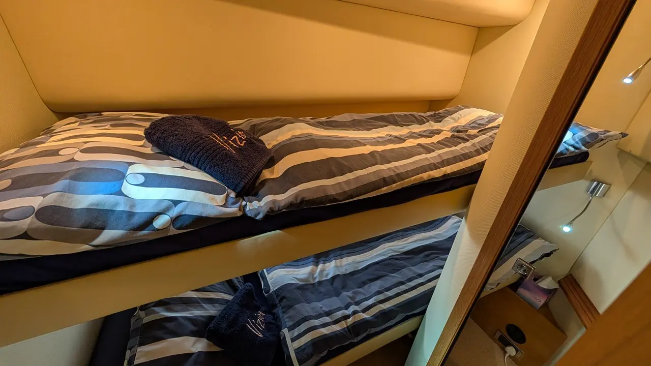 Bunk beds with striped bedding and towels in a cosy room, featuring bedside lighting and a mirror reflection.