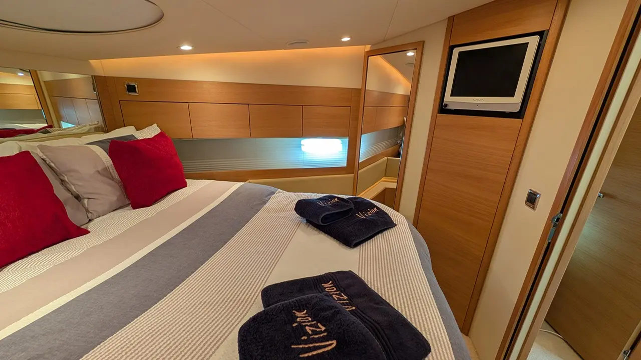 Luxury bedroom with striped bedding, red cushions, navy towels, and a wall-mounted TV, featuring warm wood paneling.