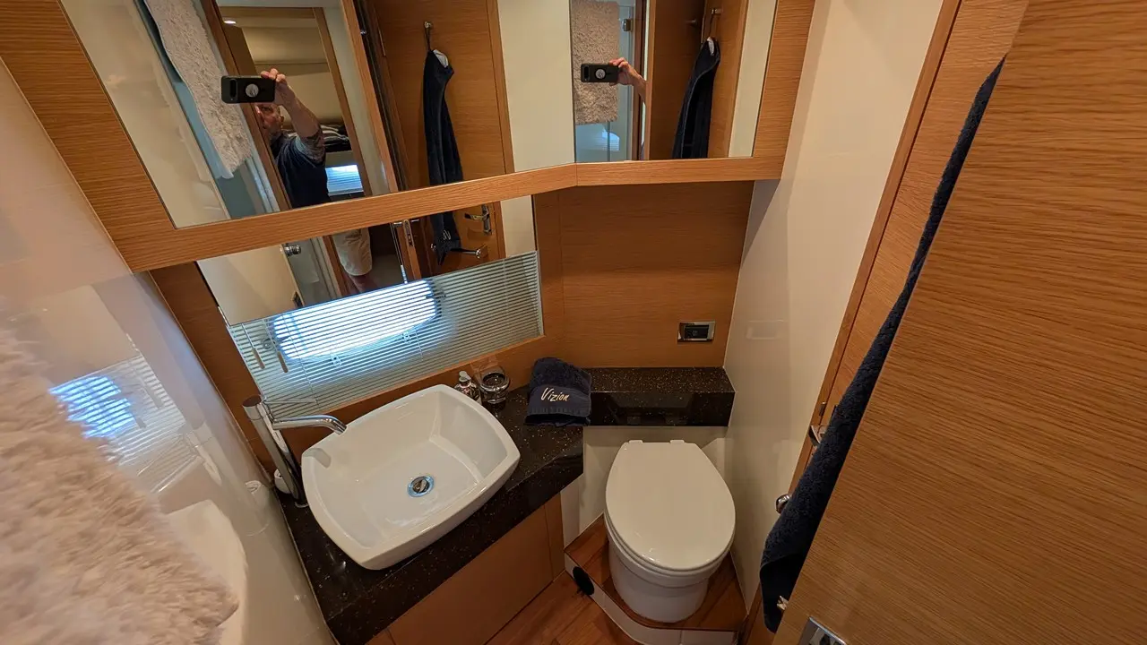 Modern bathroom interior featuring a sink, toilet, mirror, and a towel, set against wooden finishes and ambient lighting.