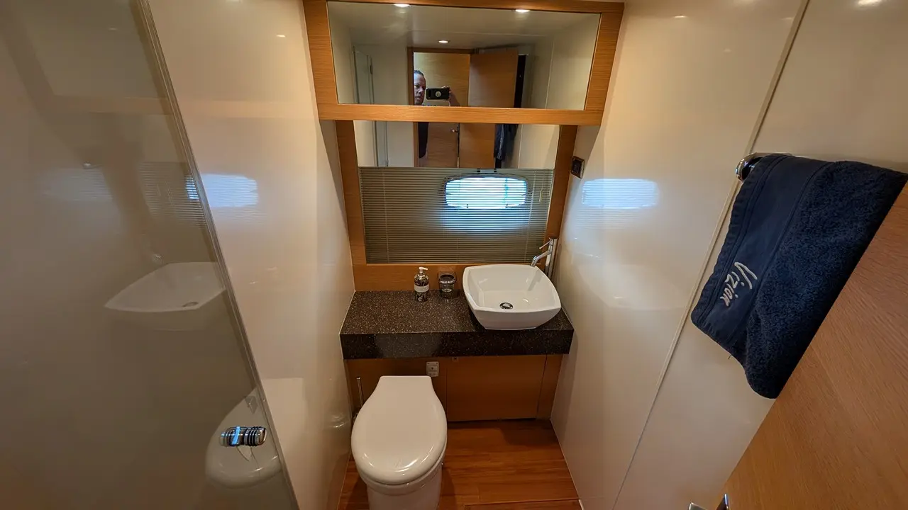 Stylish boat bathroom featuring a modern basin, toilet, wooden accents, and a large mirror with a view window.