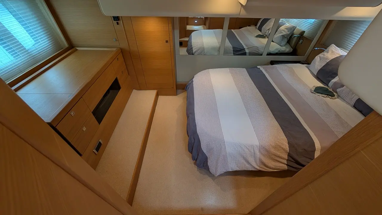 Modern bedroom interior featuring a striped bedspread, wooden furniture, and a mirror reflecting the bed and decor.