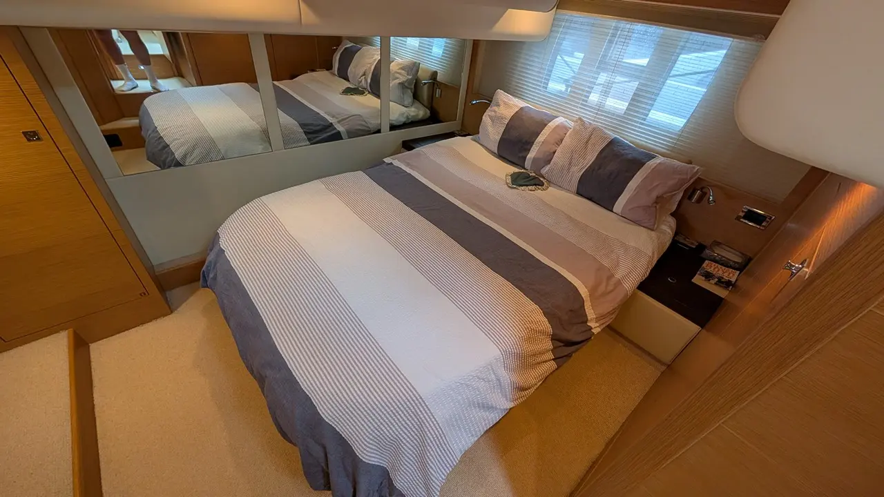 Modern bedroom with a striped duvet, bedside tables, and a large mirror reflecting natural light.