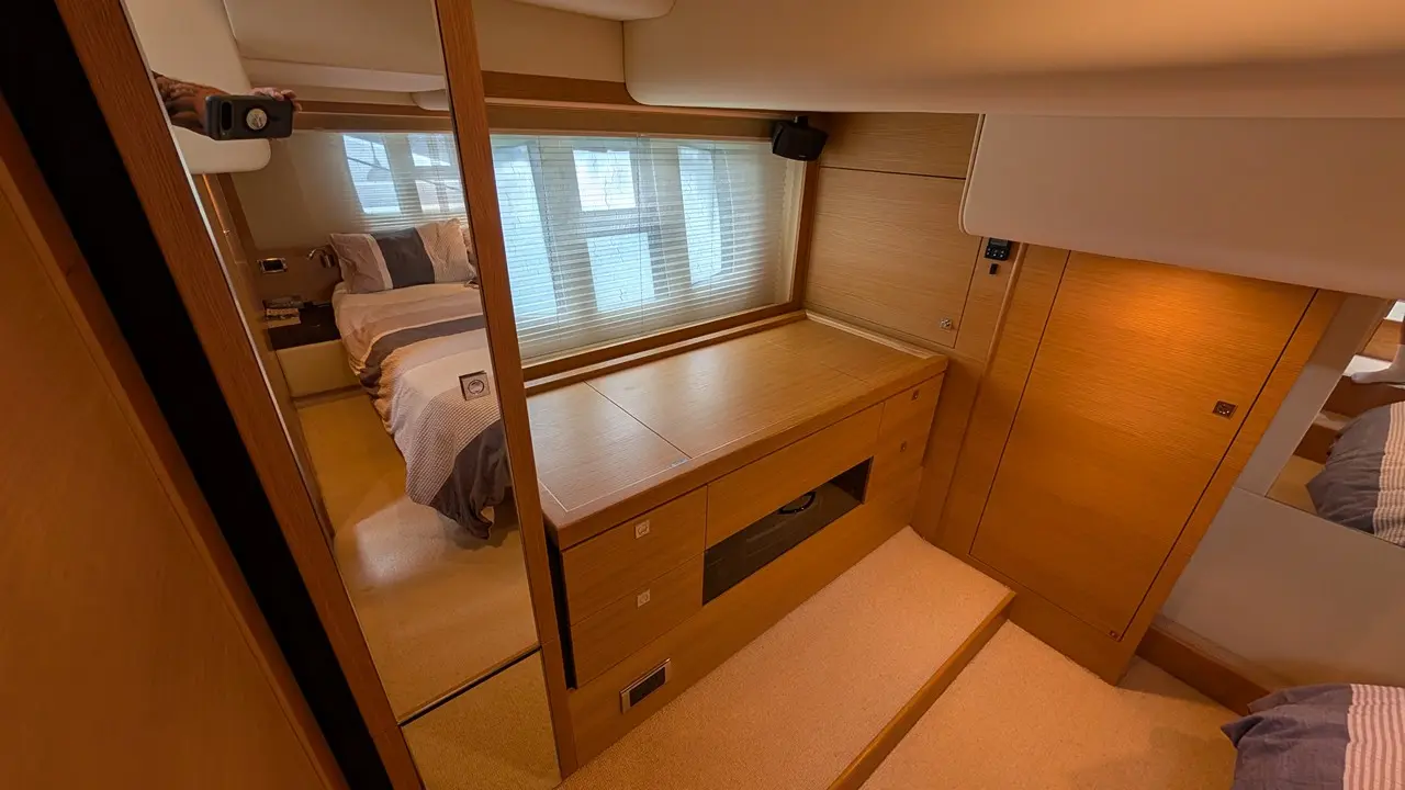 Luxurious cabin interior featuring a double bed, wooden storage unit, and large window with blinds. Soft lighting enhances ambiance.