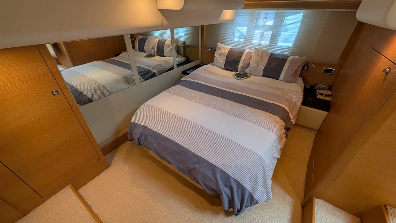 Modern yacht bedroom featuring a double bed with striped bedding, wooden furnishings, and a reflective wall.