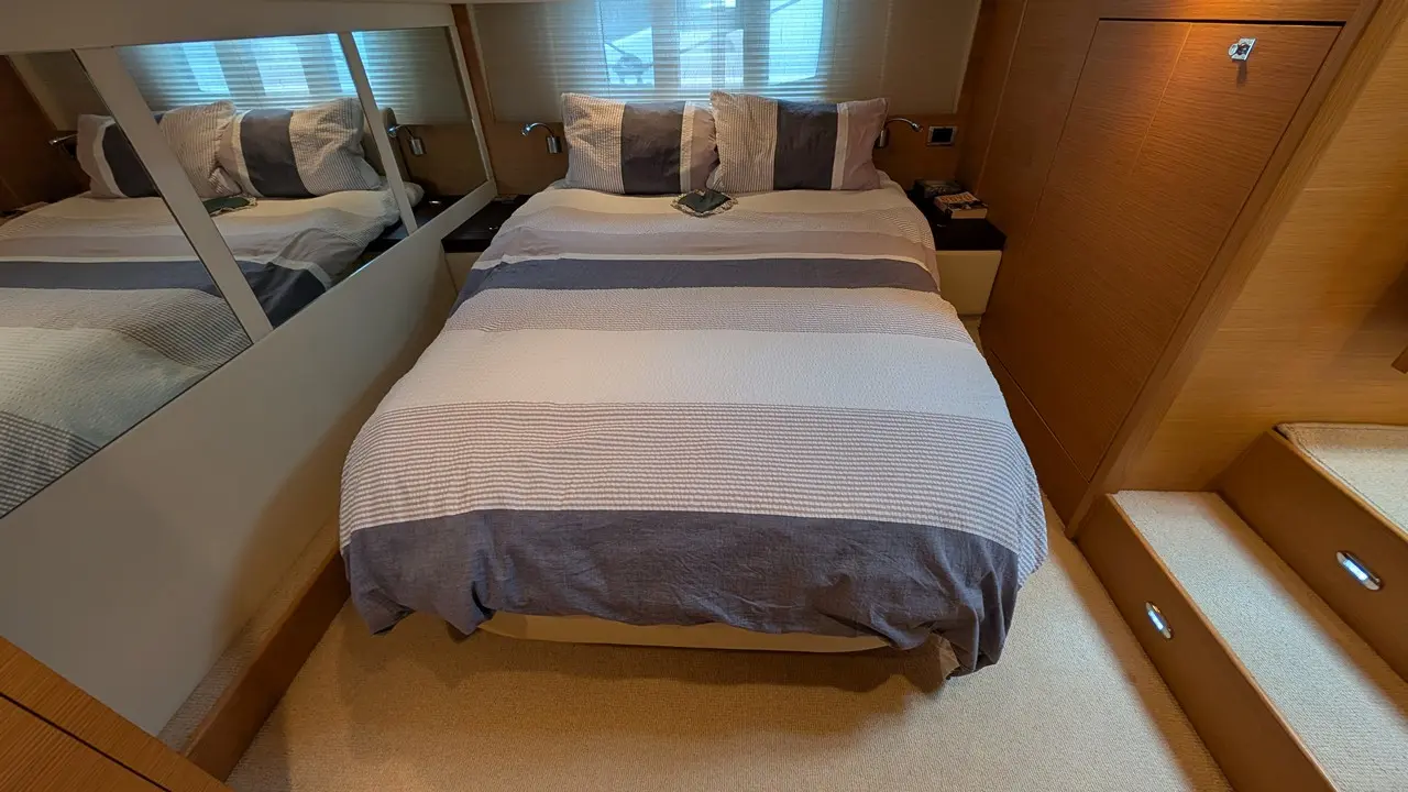 Modern bedroom with a striped duvet, mirrored wall, bedside lights, and stairs, highlighting a compact, stylish design.