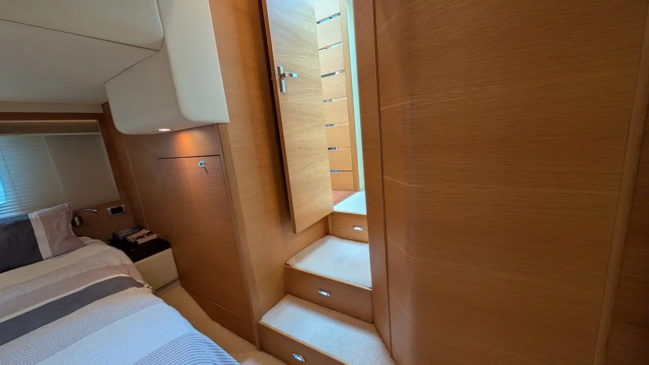 Modern boat cabin featuring a staircase, wooden walls, and a bed. A door opens to a well-lit area above.