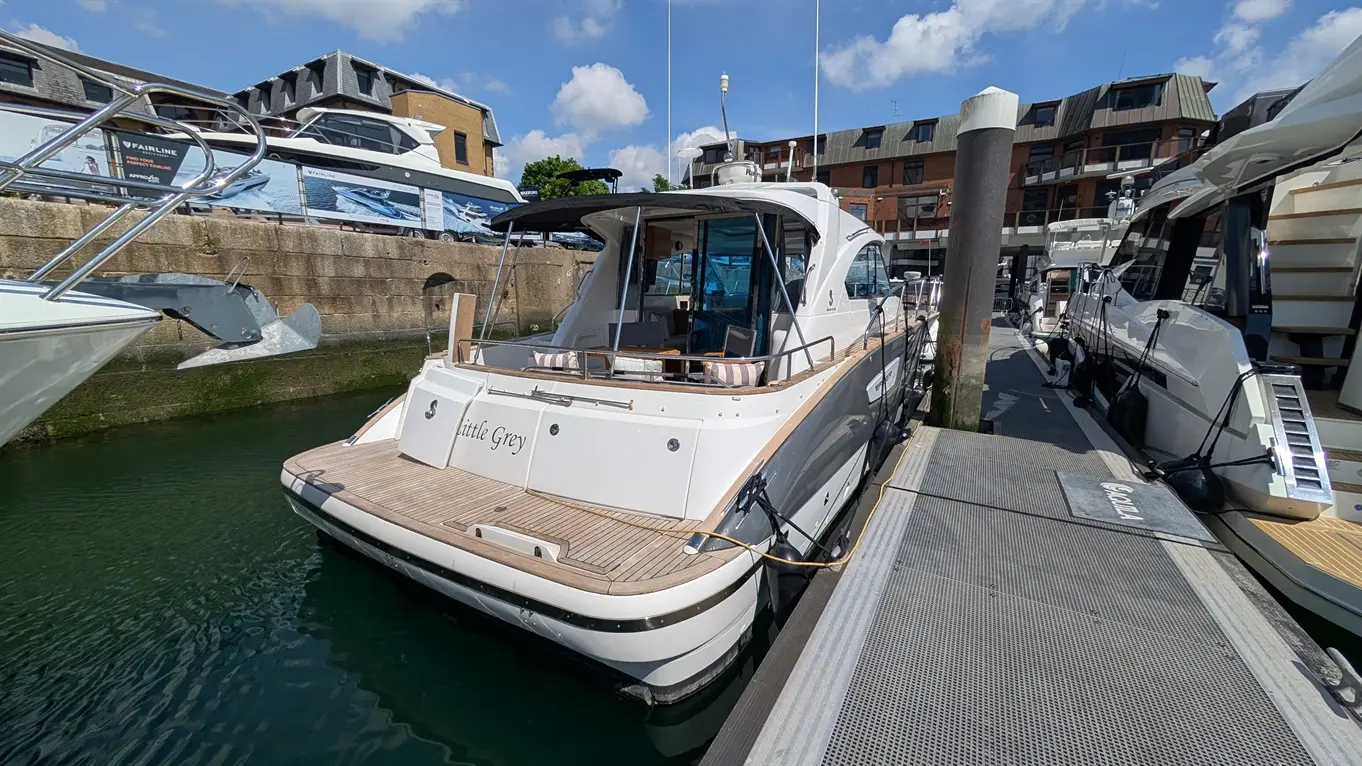 Luxury motorboat "Little Grey" docked by the marina, surrounded by other vessels, under a bright blue sky with clouds.