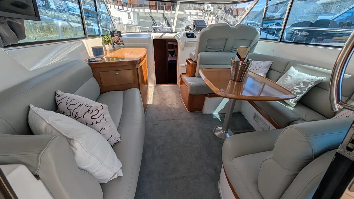 Interior of a modern yacht, featuring leather seating, a wooden table, and a smart TV, with sunlight illuminating the space.