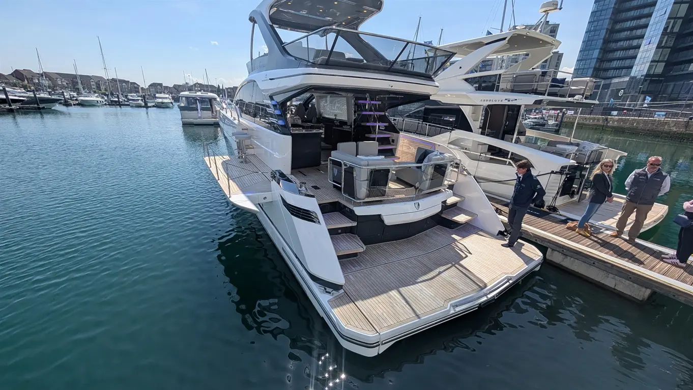 Luxury yacht docked at a marina, showcasing an elegant deck, seating areas, and nearby people enjoying the waterfront view.
