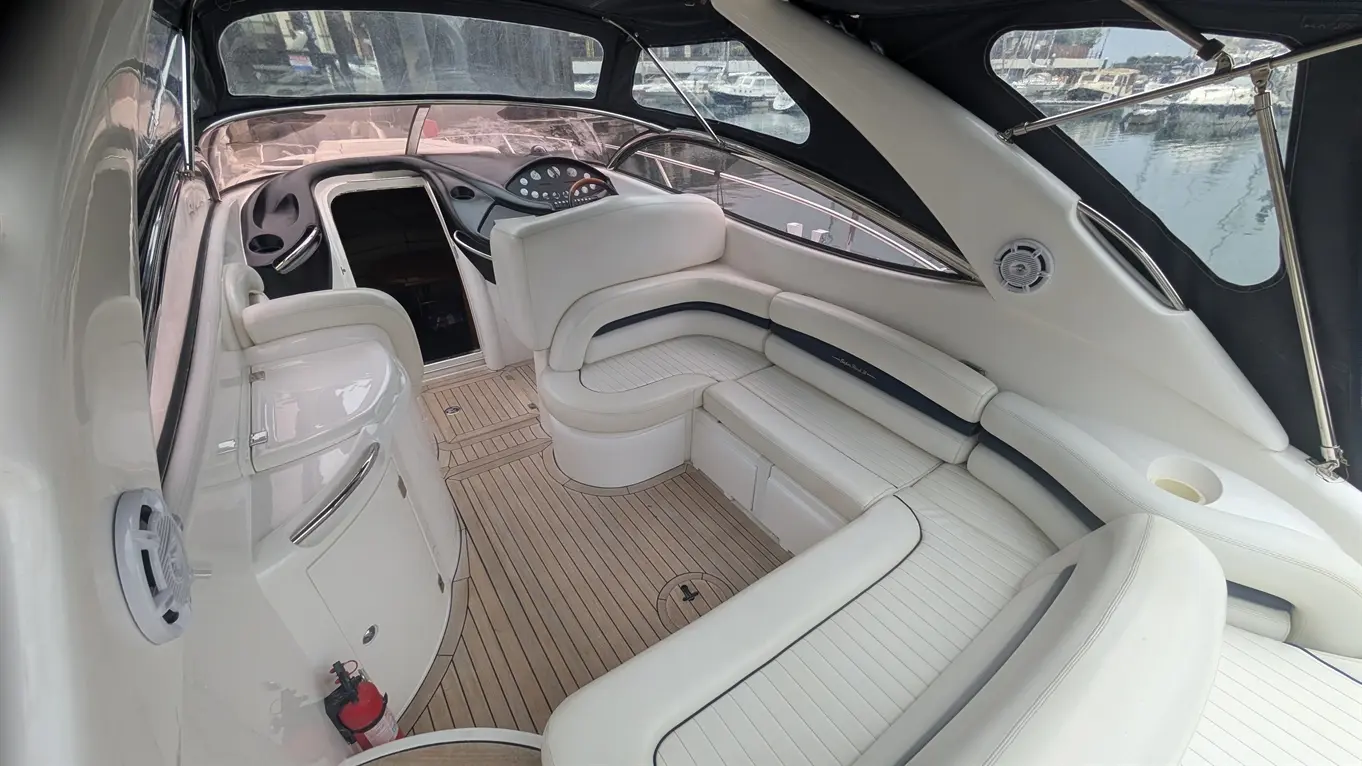 Spacious interior of a luxury boat featuring white leather seating, wooden flooring, and a dashboard with navigation instruments.
