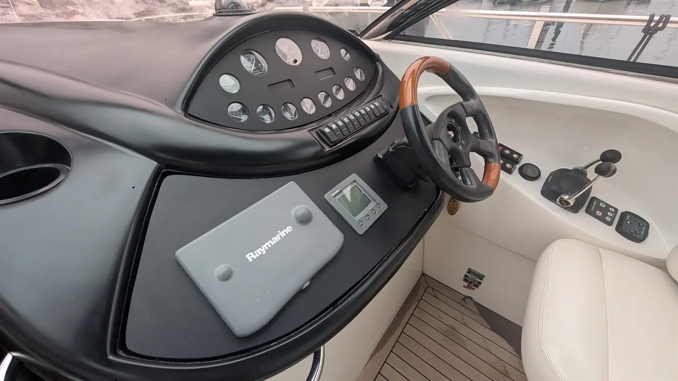 Boat dashboard with steering wheel, Raymarine device, gauges, and controls, showcasing nautical instrumentation and design.