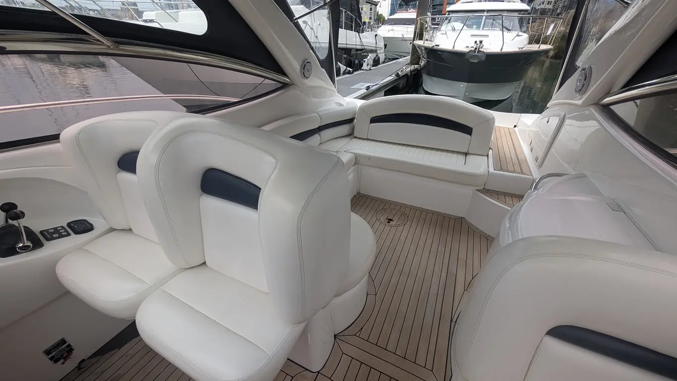 Interior of a boat featuring white leather seating, a wooden floor, and a view of other boats moored outside.