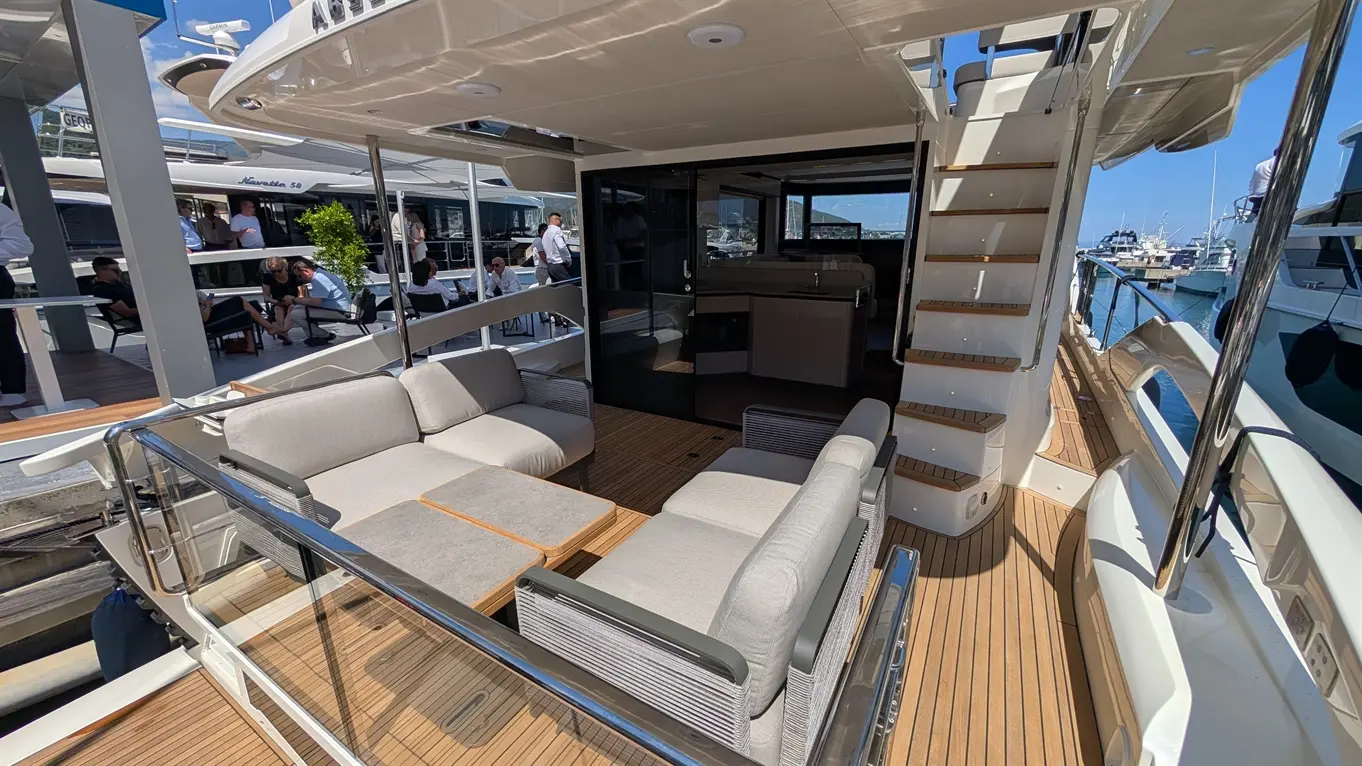 Luxury yacht deck featuring modern seating, a staircase, and an interior view. Nearby people enjoying the marina atmosphere.