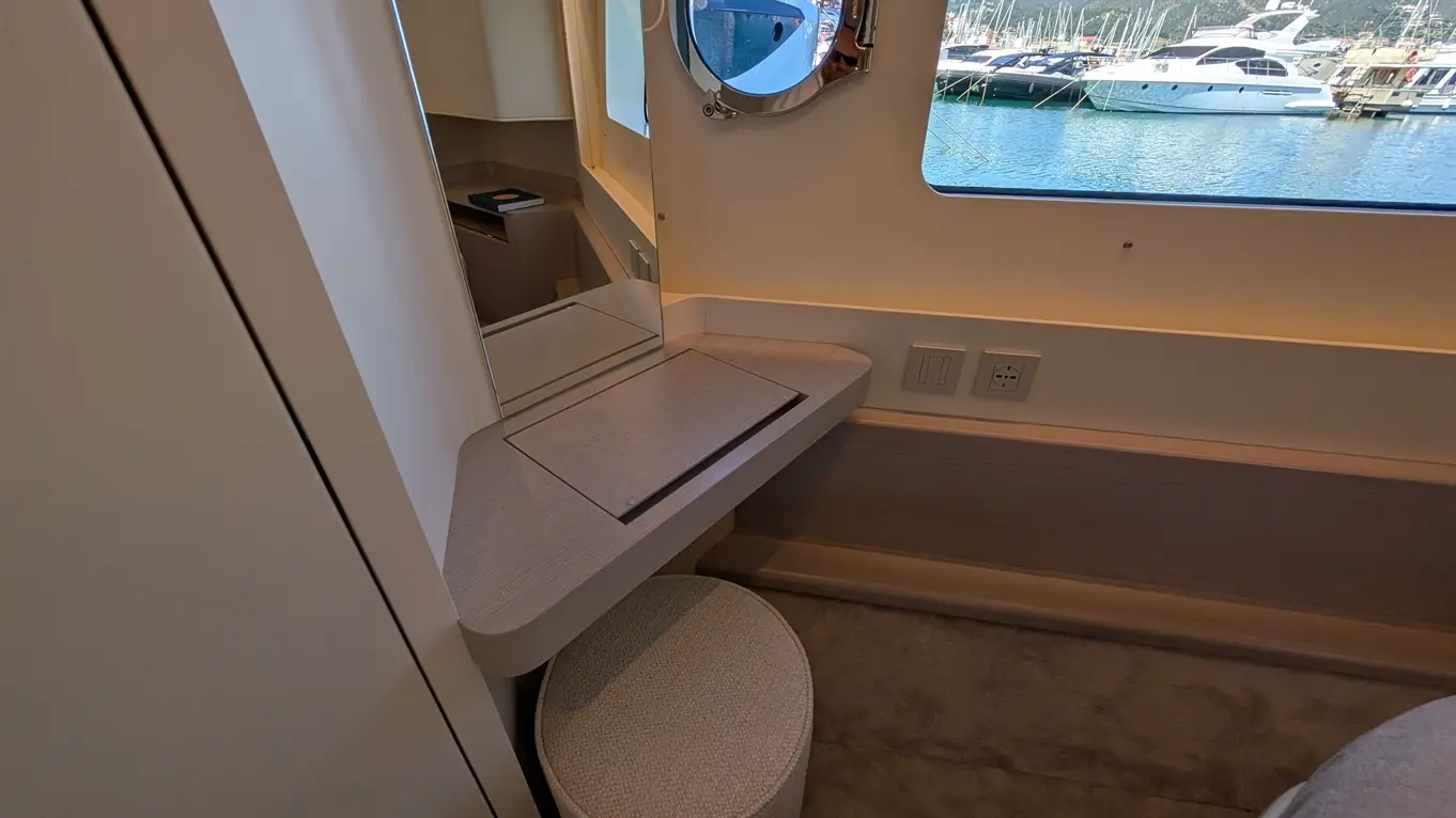 A modern cabin interior with a sleek desk, circular stool, mirror, and a view of a marina through a large window.