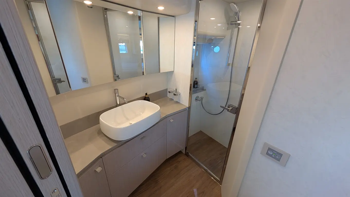Modern bathroom featuring a glass shower, a white basin on a grey counter, and multiple mirrors reflecting natural light.