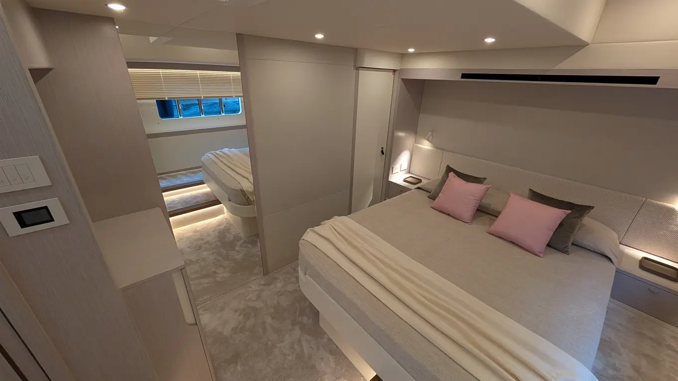 Modern bedroom with a queen bed, two pink cushions, and ambient lighting; a mirror reflects light and bedding details.