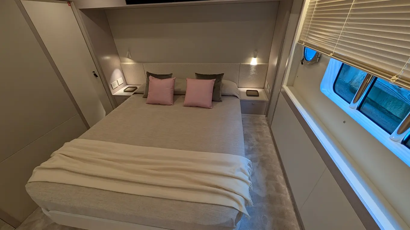 Modern bedroom featuring a double bed with pink and grey pillows, soft blankets, bedside lights, and a window.