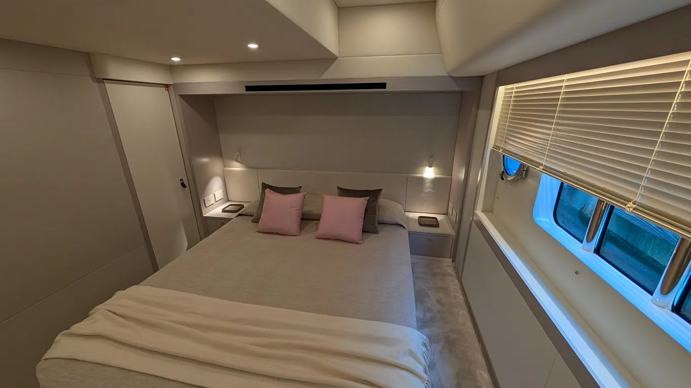 Modern bedroom featuring a double bed with pink and grey cushions, soft lighting, and a window with blinds.
