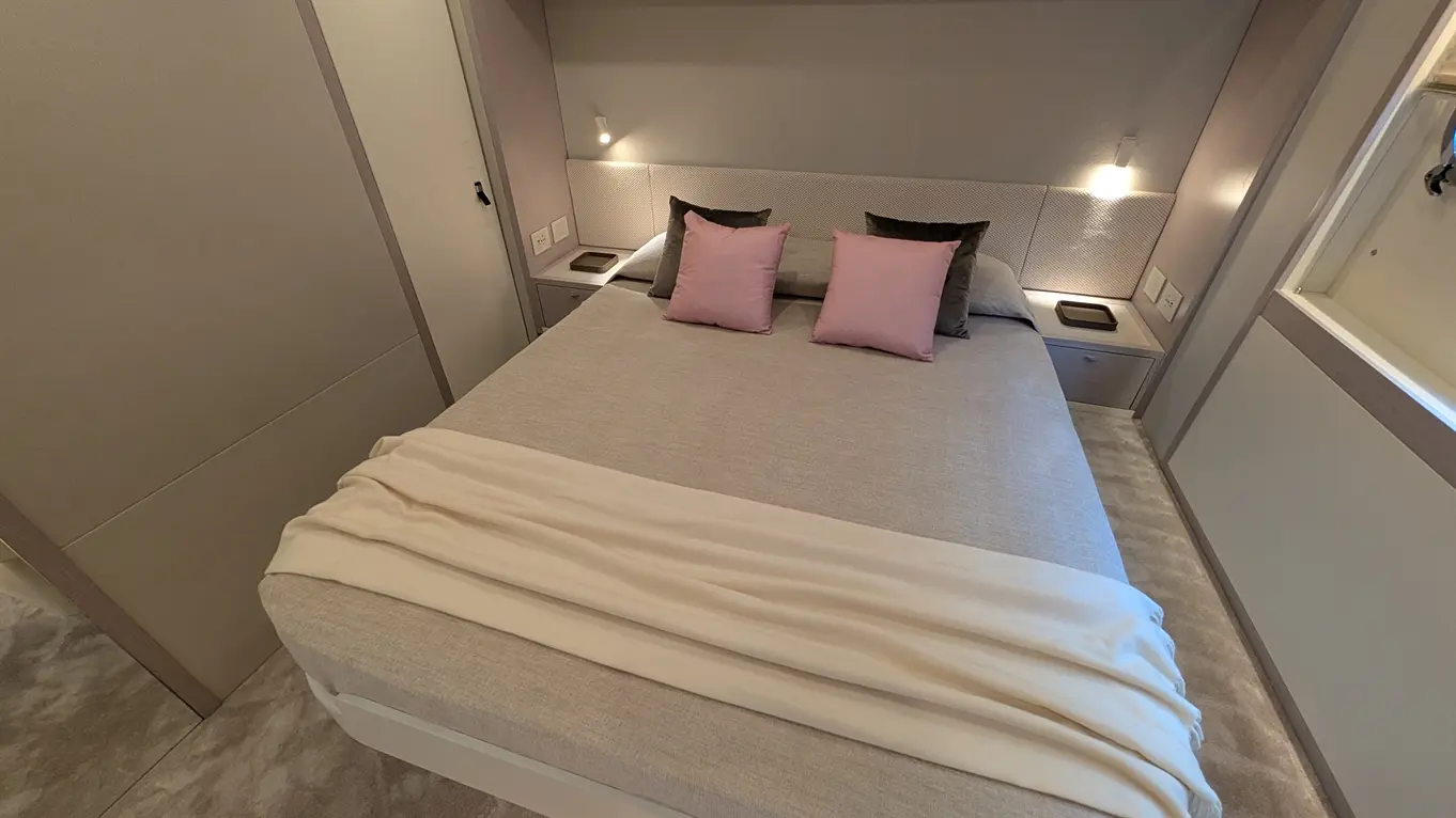 A modern bedroom featuring a double bed with grey bedding, pink cushions, and soft lighting, alongside minimalist furniture.
