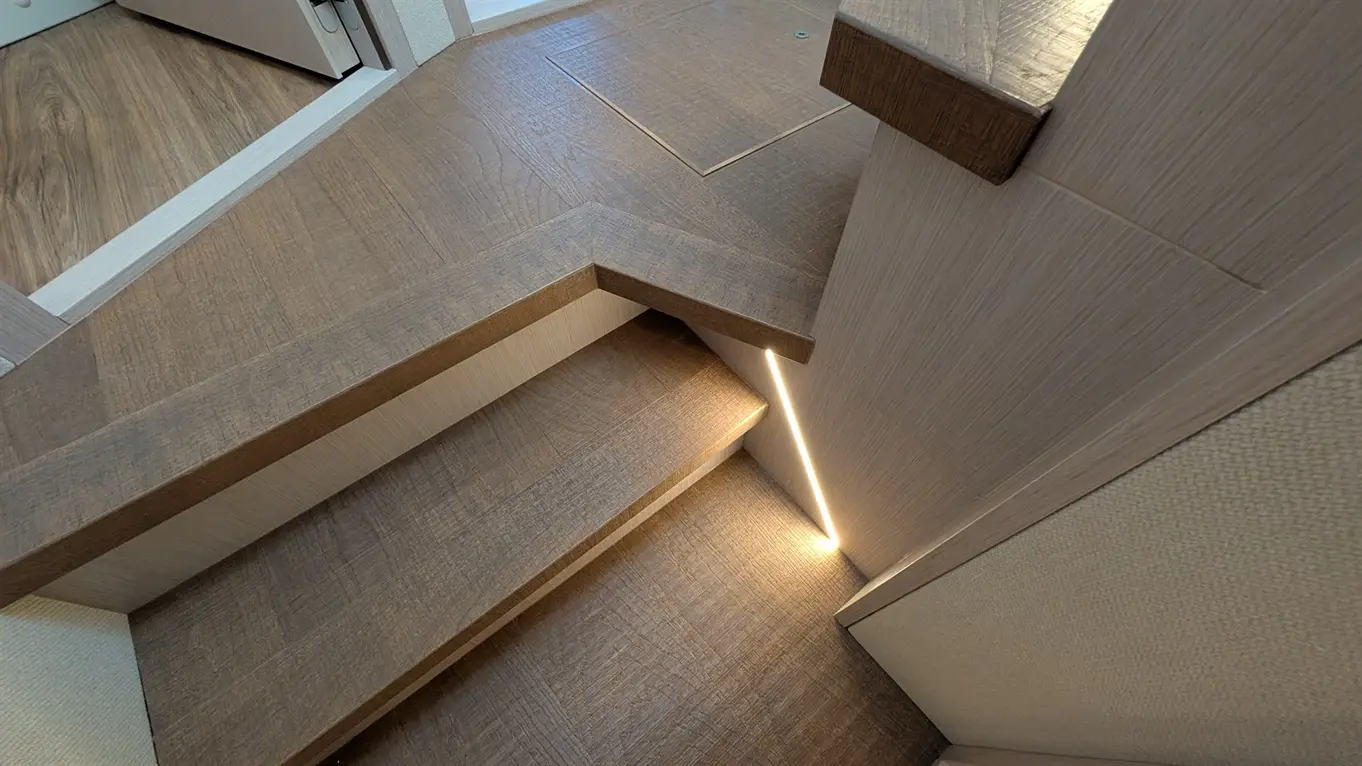 Wooden staircase with soft lighting, showcasing textured flooring and a subtle corner view of an interior space.